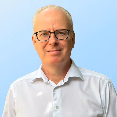 Middle-aged man with glasses and short hair wearing a white collared shirt against a blue background.