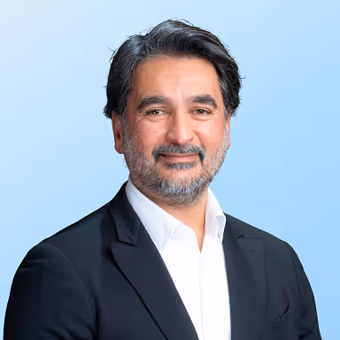 Smiling man with salt-and-pepper hair and beard wearing a black blazer and white shirt.