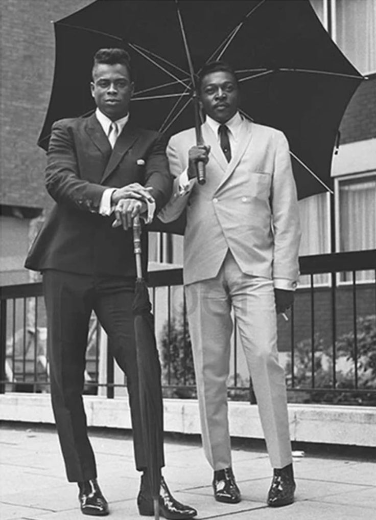 Black-and-white photograph of two well-dressed Black men in suits standing under an umbrella.