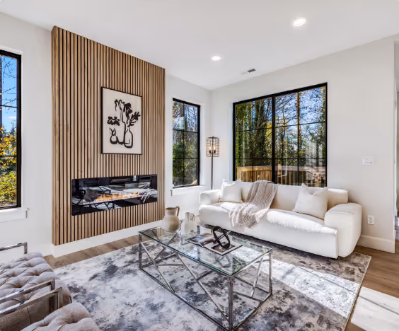 Bright modern living room with white sofa, glass coffee table, and wall-mounted electric fireplace under wood paneling.