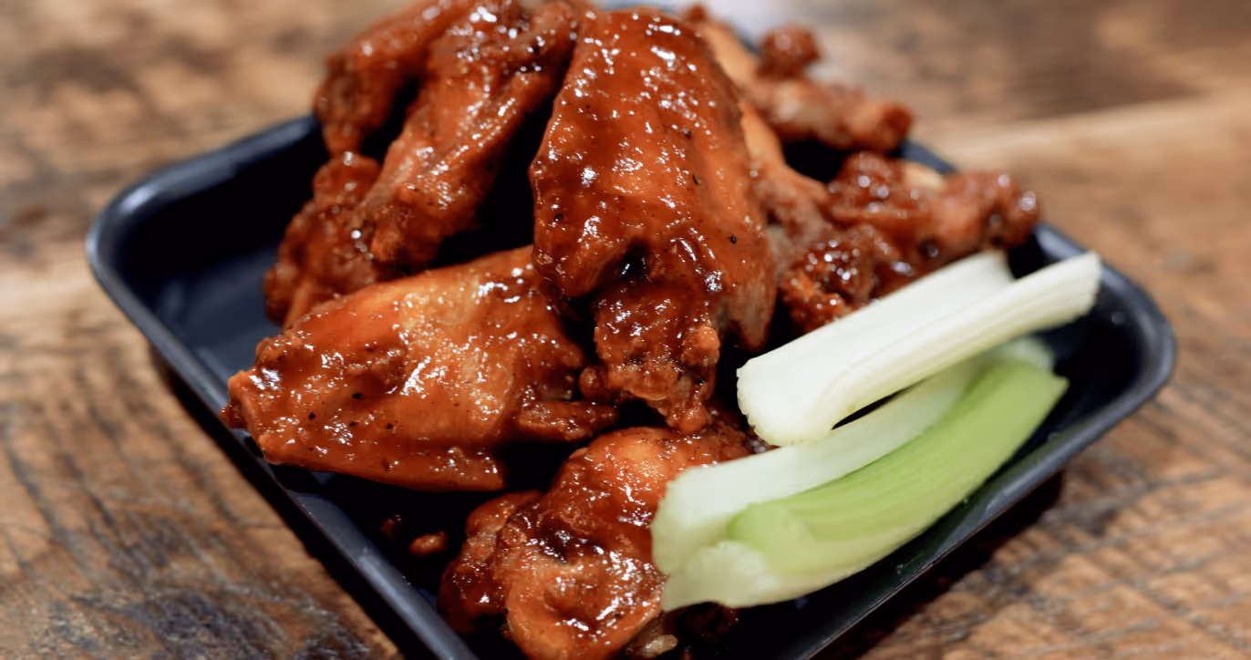 Eight traditional wings in sauce with celery sticks on a black tray.