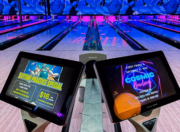 View of a bowling alley with lane screens displaying promotions for daytime practice specials and cosmic bowling events.