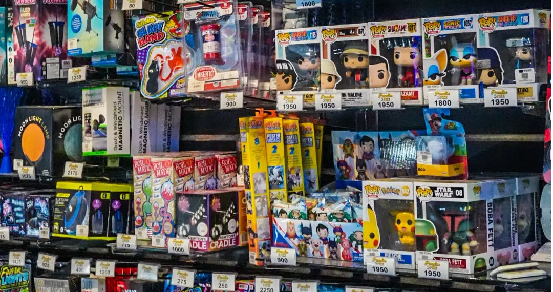 Shelf filled with various arcade prizes including Funko Pop figures, toys, and gadgets with visible price tags.