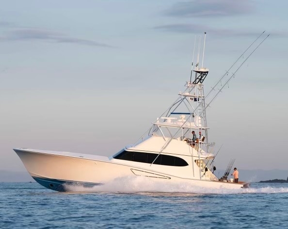 White sport fishing boat speeding on calm sea water with two people on board during daylight.