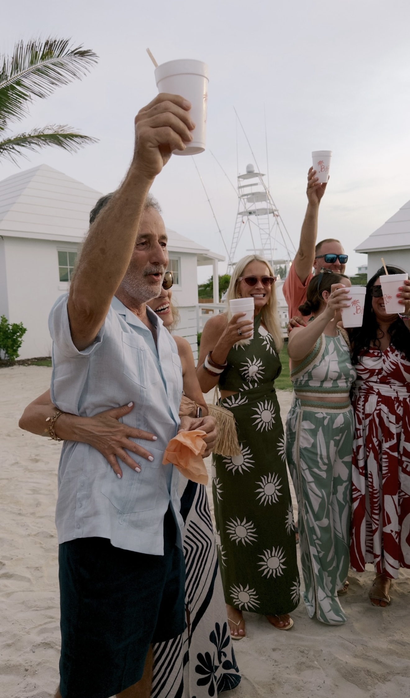 Group of people on the beach raising white cups in a celebratory toast during daytime.