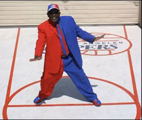 Man wearing a suit split into red and blue halves standing on a basketball court with a Los Angeles Clippers logo.