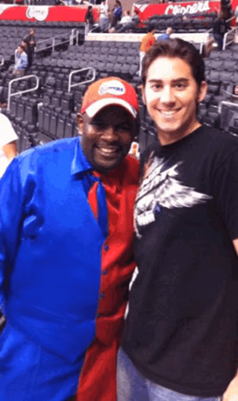Two men smiling and posing together in a stadium with empty seats in the background.