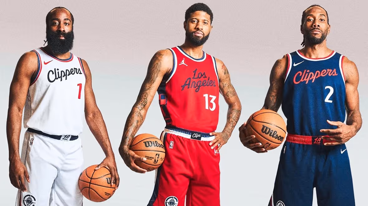 Three basketball players standing side by side wearing Los Angeles Clippers uniforms in white, red, and navy blue while holding basketballs.