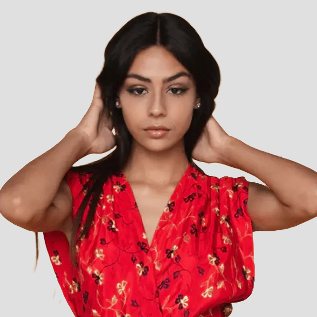 Woman with long dark hair wearing a red floral dress with hands behind her head.