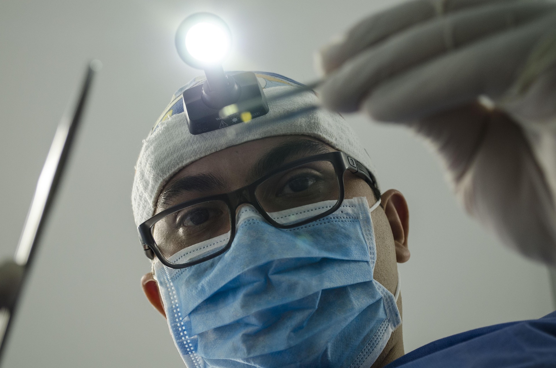 Dentist wearing glasses, surgical mask, gloves, and headlamp, performing a dental procedure.