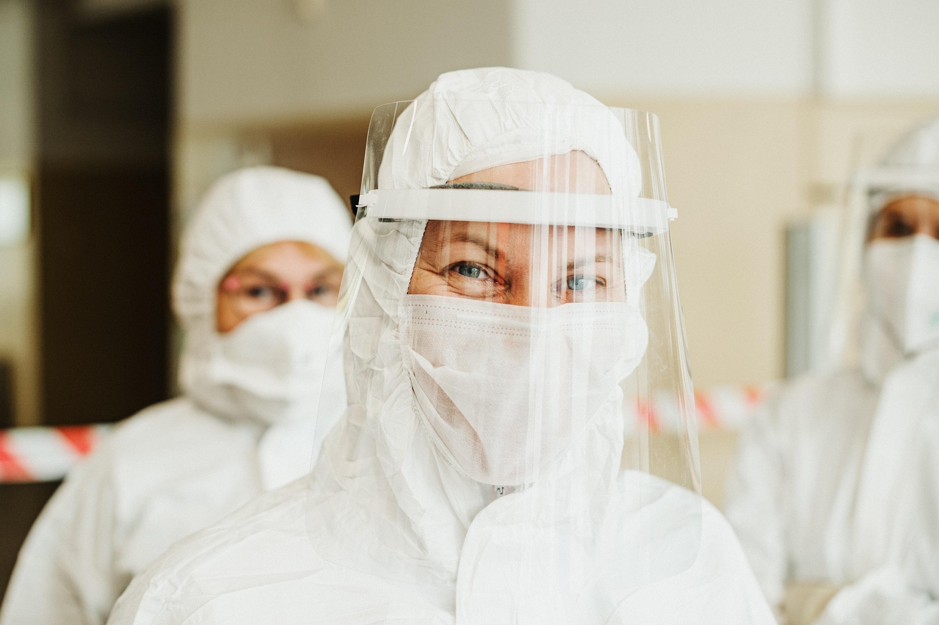 Three healthcare workers wearing white protective suits, face masks, and face shields.