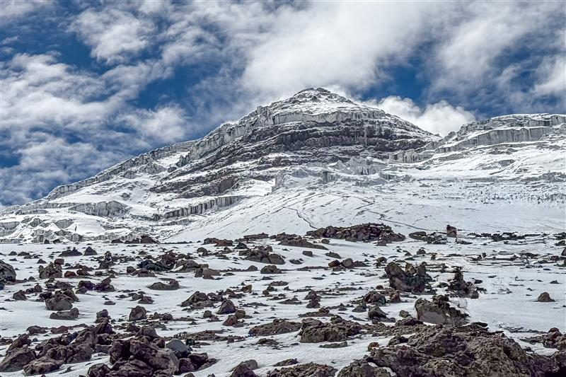 Snow-covered rocky mountain under a partly cloudy blue sky.
