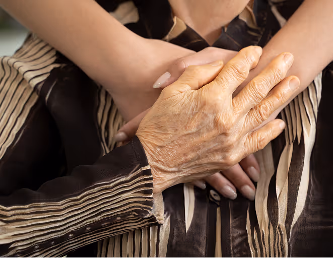 Older hand resting gently on younger crossed hands over striped clothing.