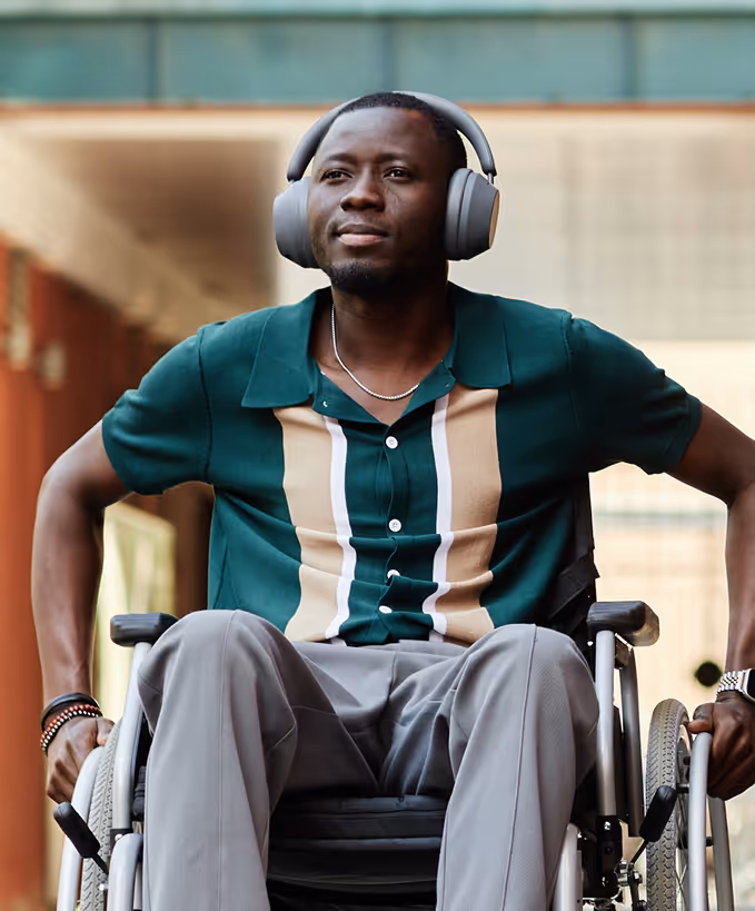 Man in a wheelchair wearing gray headphones and a green shirt with beige stripes.