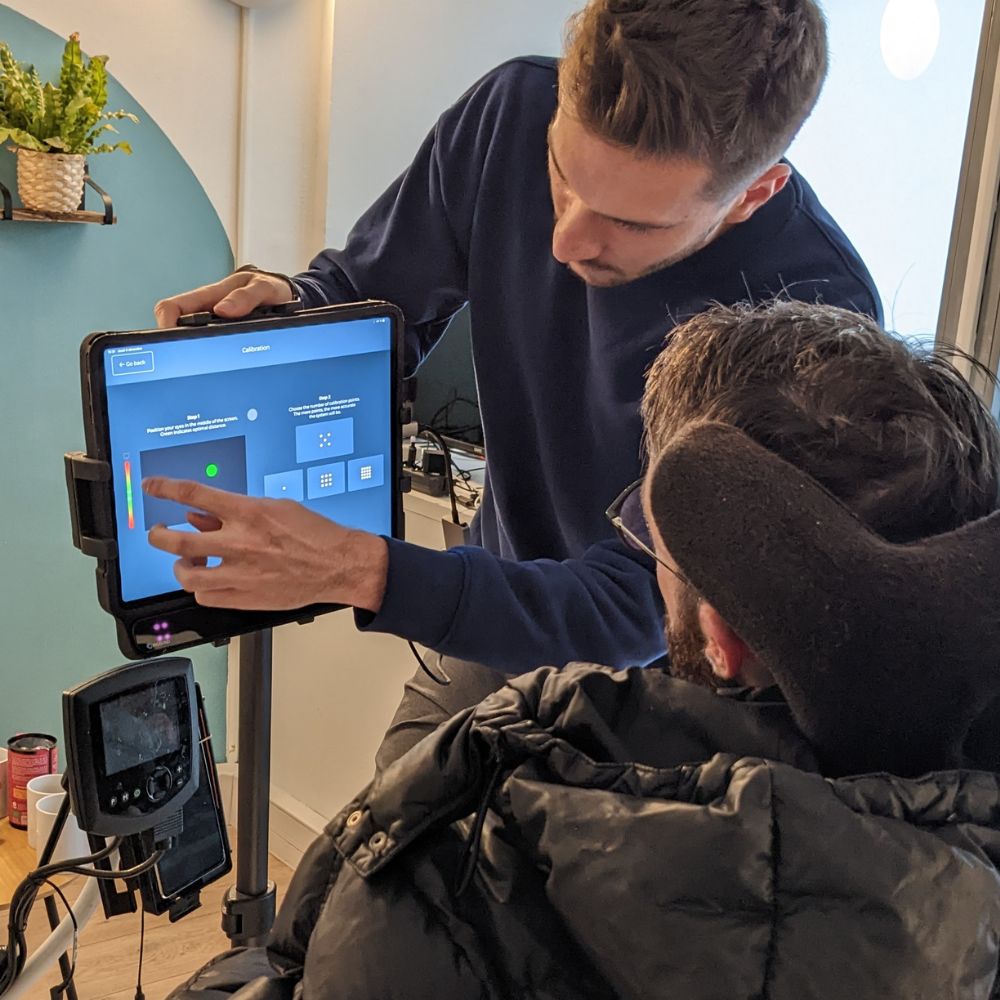 Un homme montre à une autre personne en fauteuil roulant un écran de tablette affichant une interface de calibration.
