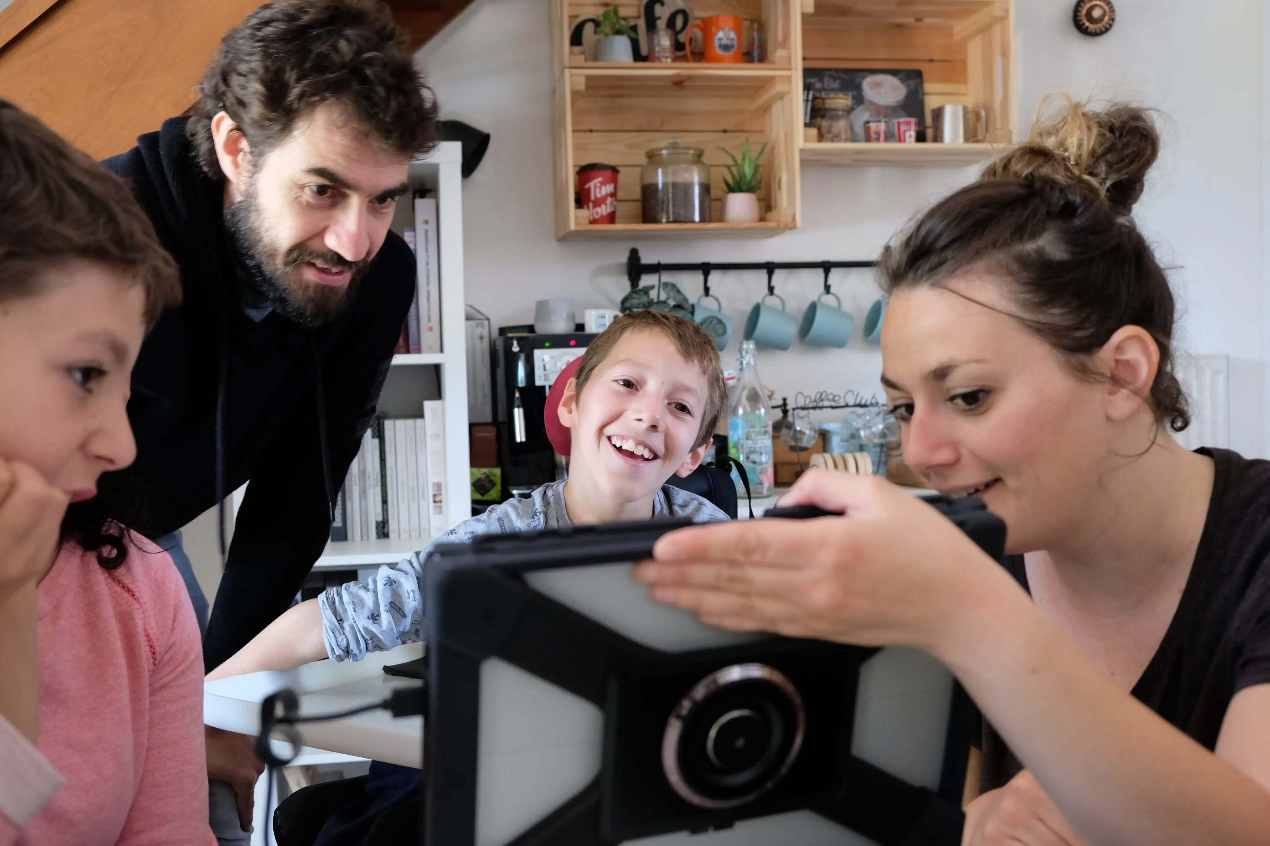 Un groupe de quatre personnes, dont un enfant en fauteuil roulant, regardent et sourient un écran sur une tablette.