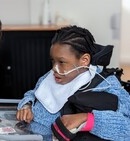 Un enfant portant un masque nasal assis dans un fauteuil roulant, tenant un téléphone portable.