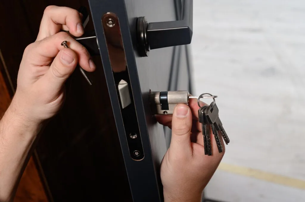 Hands repairing or installing a door lock cylinder with a set of keys visible. This emphasizes secure and efficient property management, showcasing the importance of integrating advanced access control solutions like RemoteLock for seamless operations in multifamily properties and vacation rentals.