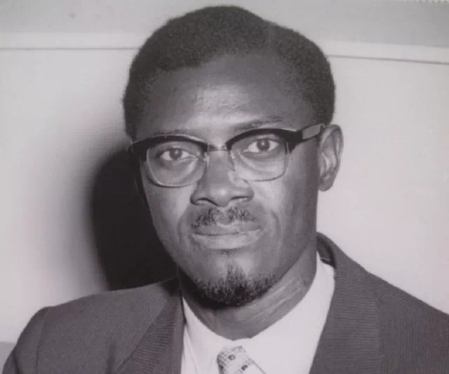Black and white portrait of a man wearing glasses, a suit jacket, shirt, and tie.