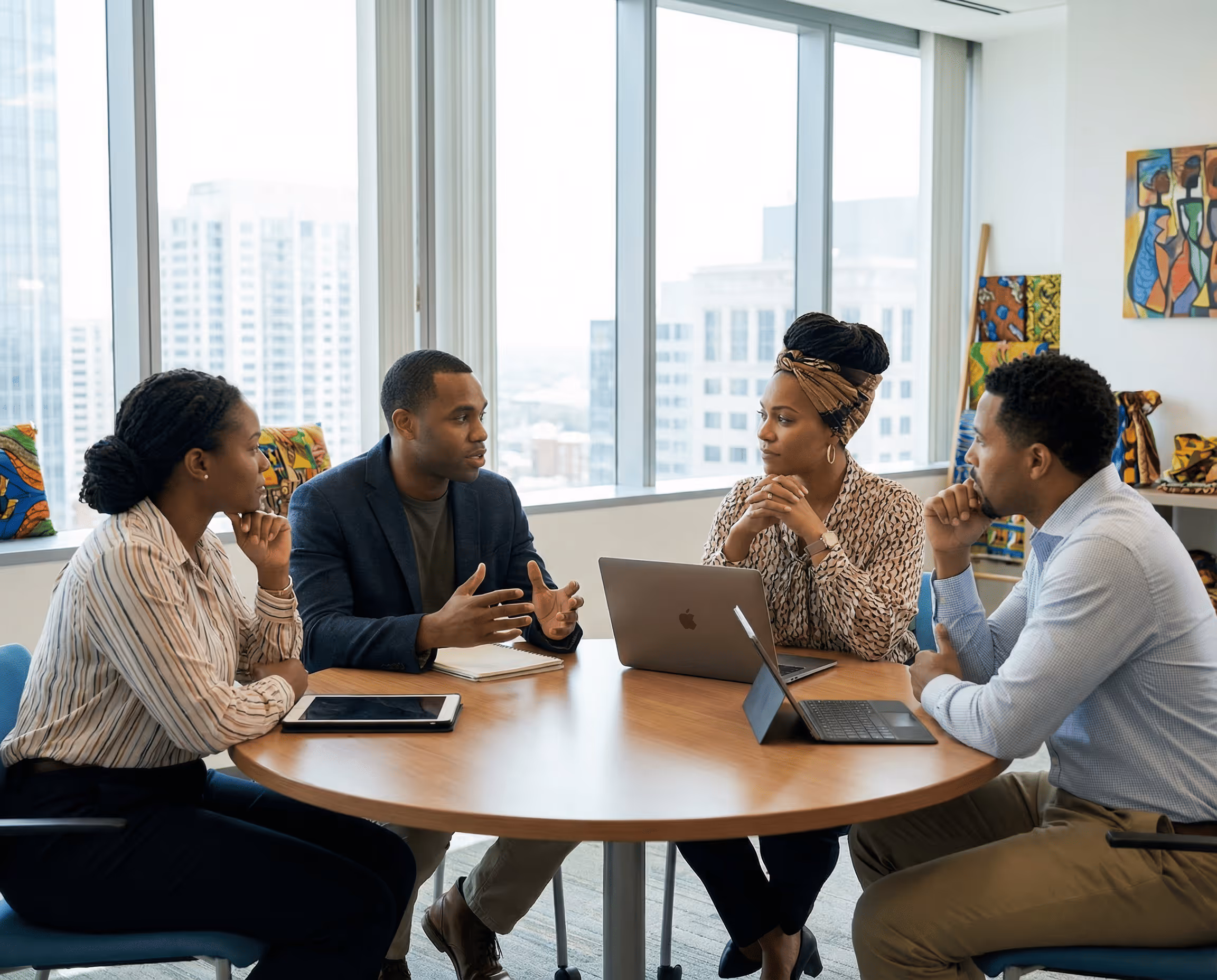 Four colleagues engaged in a discussion around a round table in a modern office with city views.