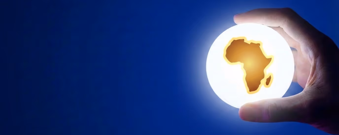 Hand holding a glowing orb with the silhouette of the African continent illuminated inside against a dark blue background.