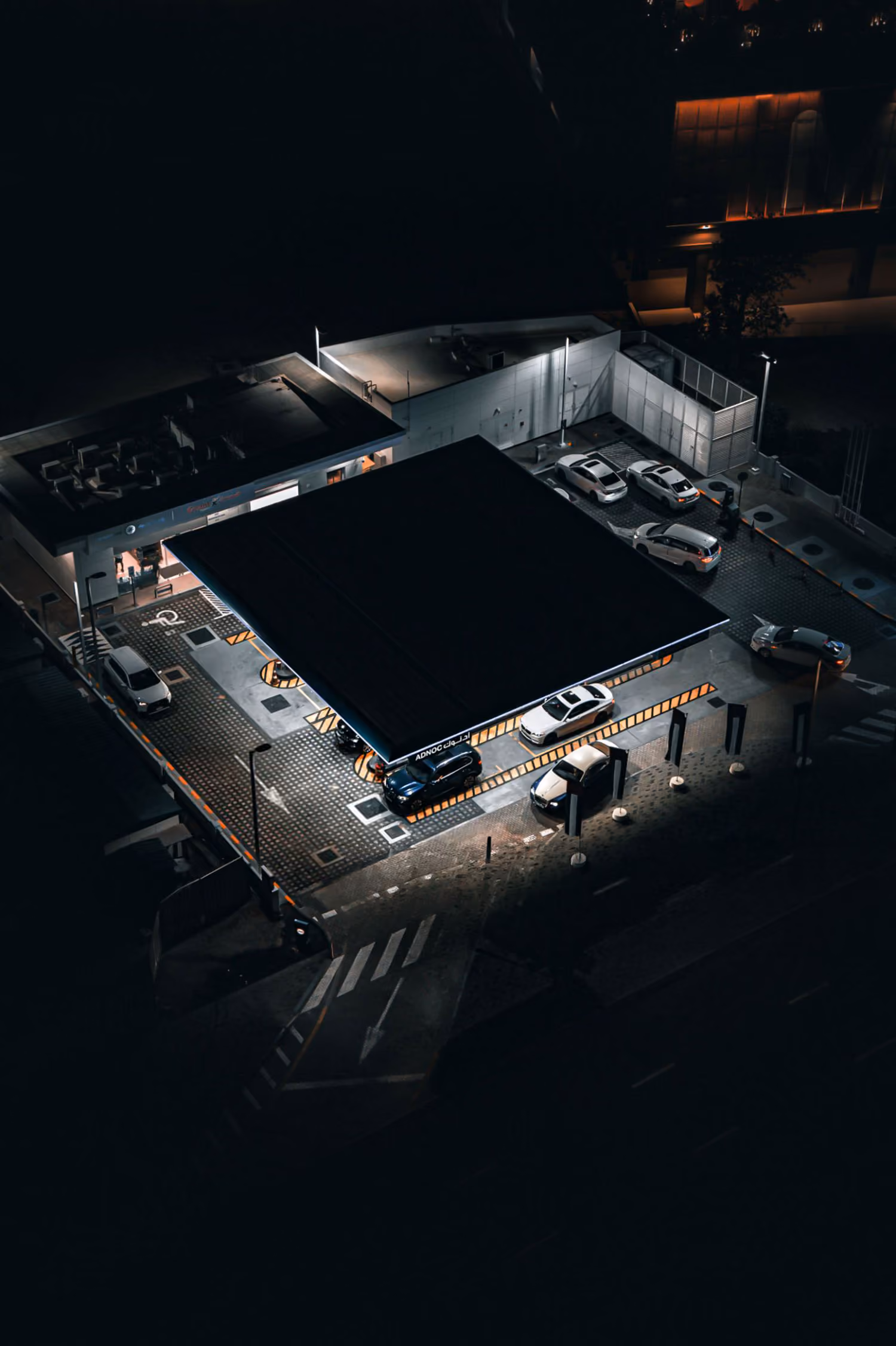 Aerial night view of a gas station with cars parked and lit by overhead lights.