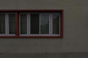A horizontal row of five windows with white frames and wooden trim on a gray exterior wall.