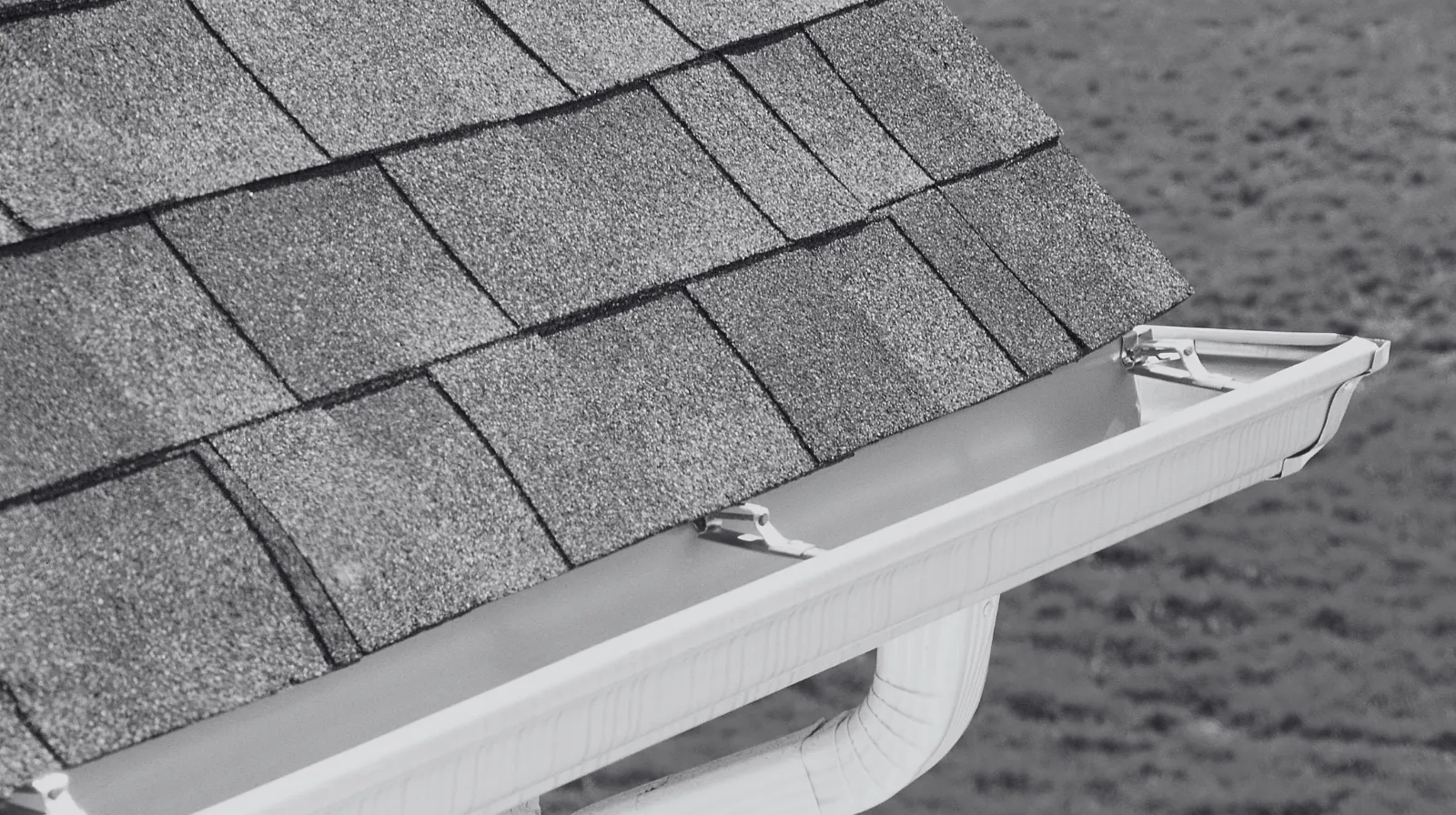 Close-up of a clean white rain gutter attached to a house roof with asphalt shingles.