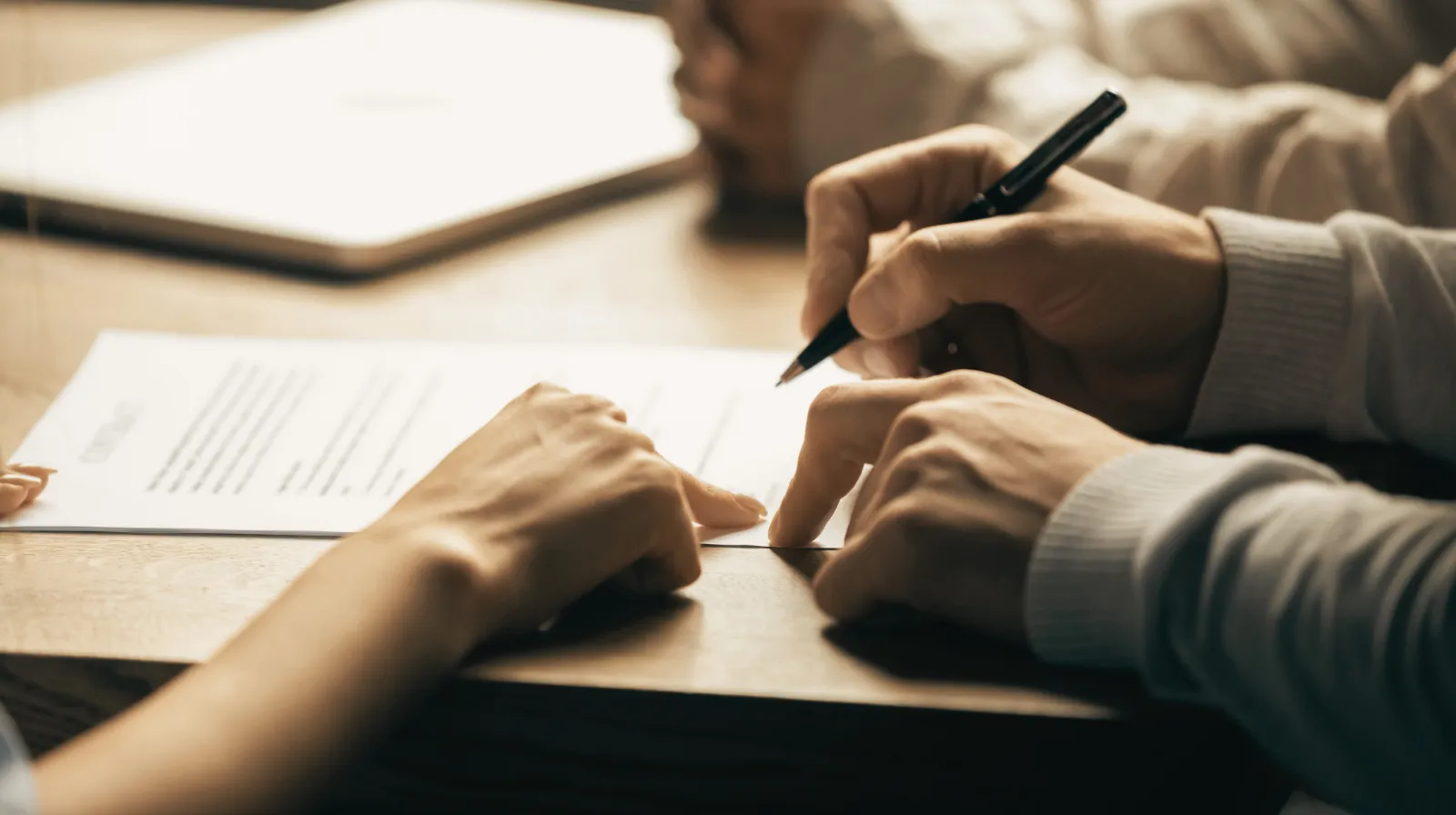 Two people reviewing and signing a contract document on a wooden table.