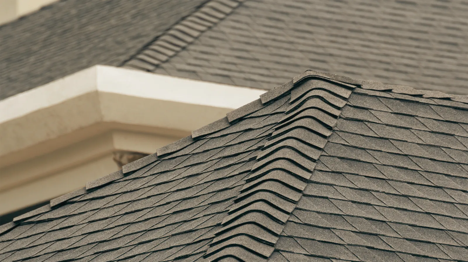 Close-up view of a gray asphalt shingle roof with a ridge cap on a residential house.