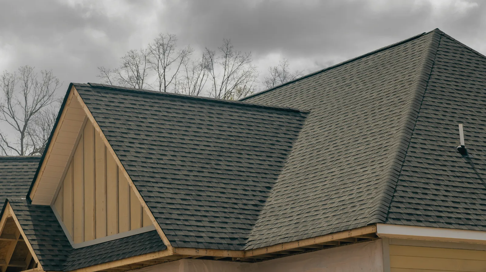 Close-up of a gray shingled roof with multiple gables under a cloudy sky.