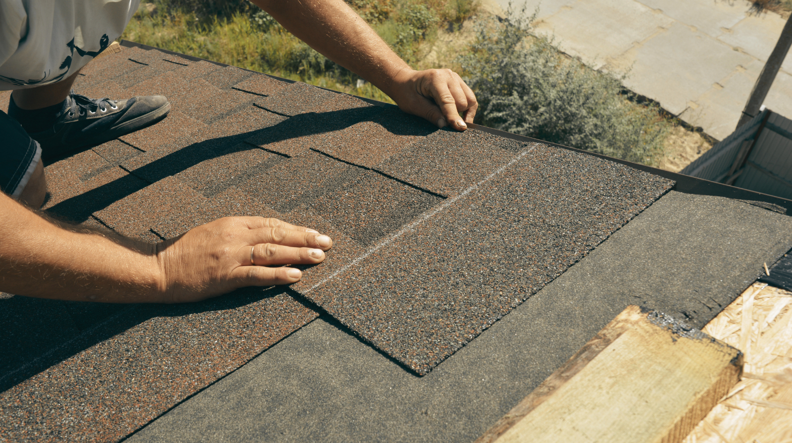 Person installing brown asphalt roofing shingles on a house roof.