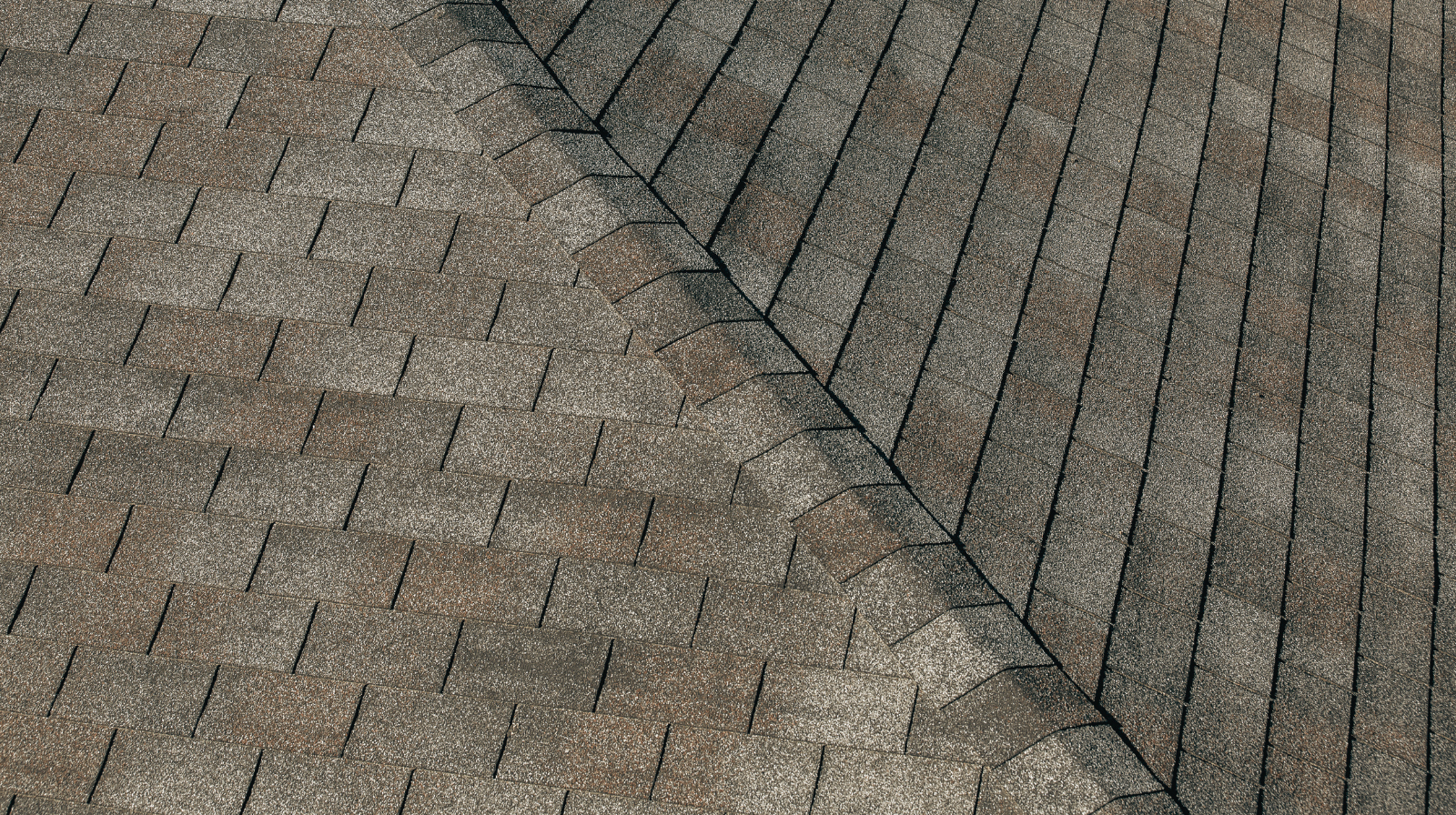 Close-up view of a roof with overlapping brown and gray asphalt shingles arranged in a staggered pattern.