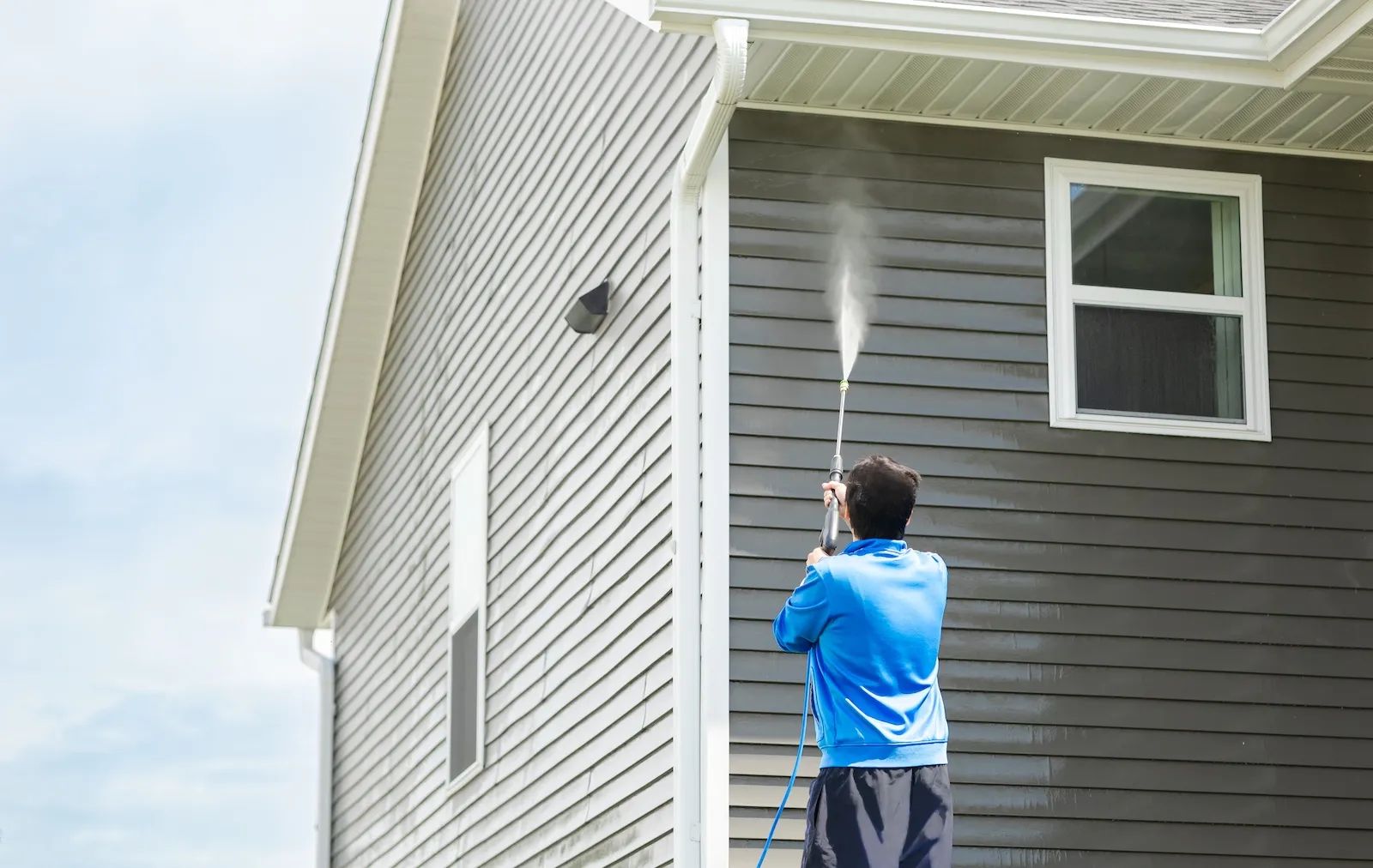 Person washing the exterior siding of a gray house.