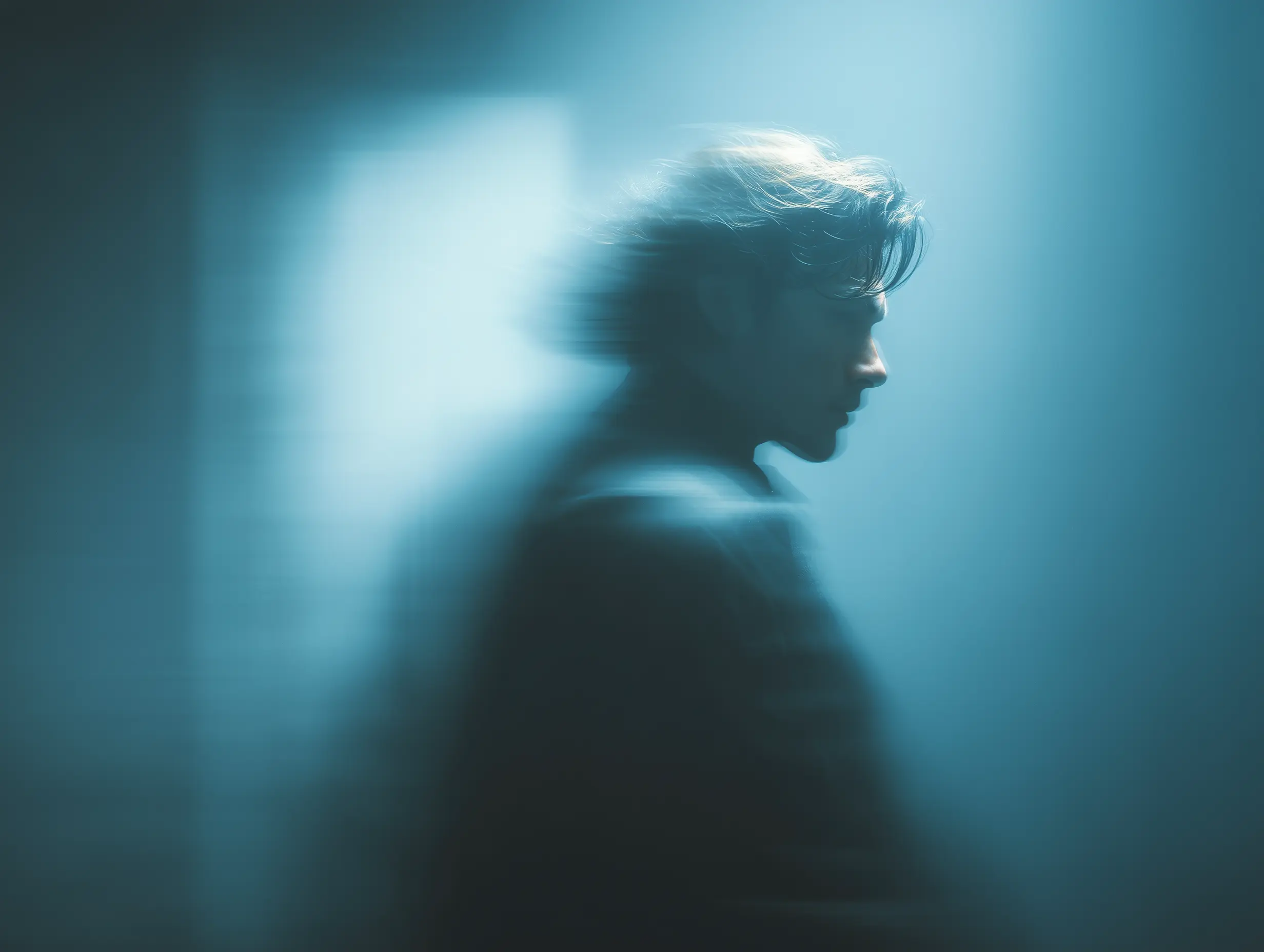 Blurred side profile of a person with wind-swept hair in a blue-toned abstract background.