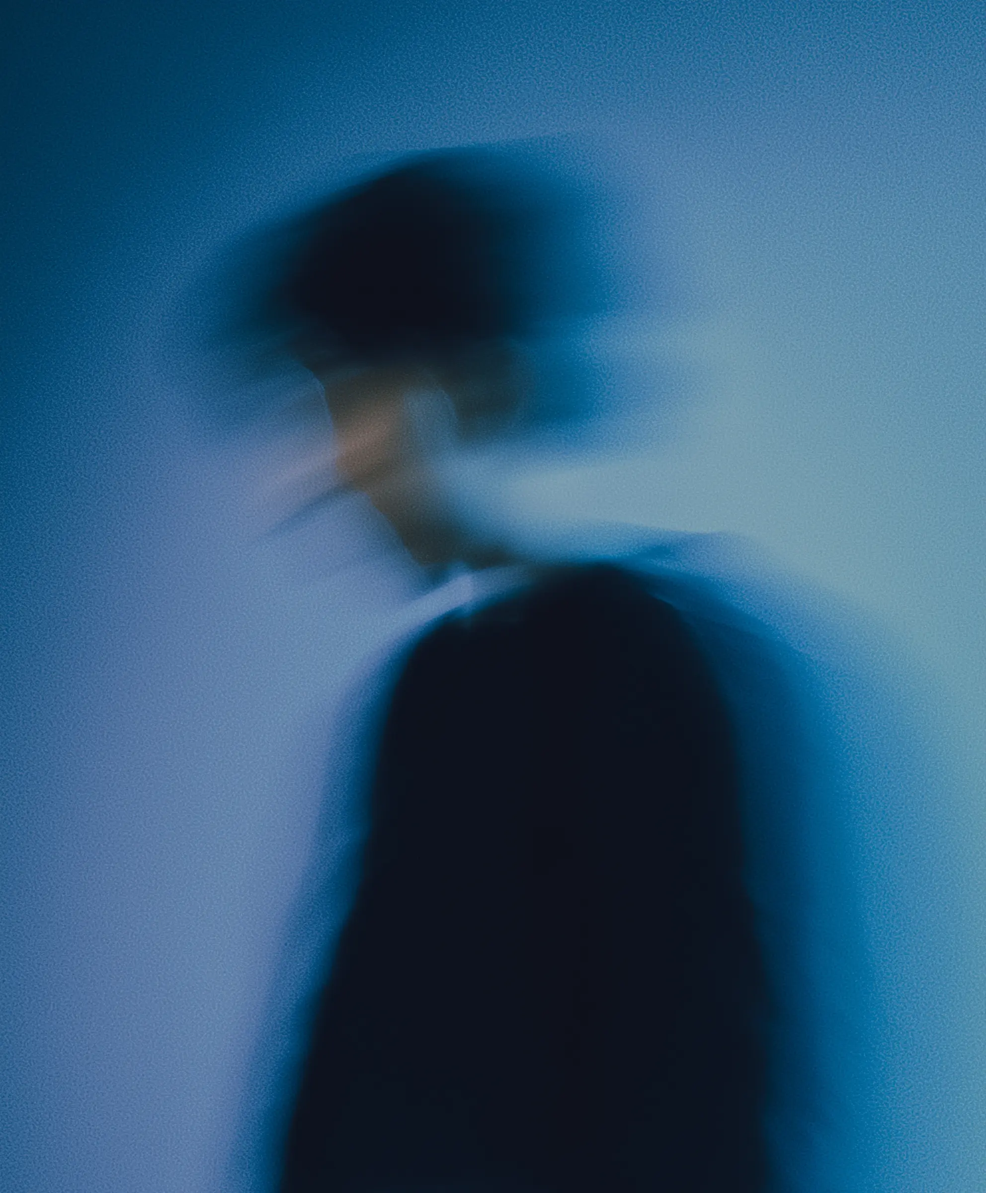 Blurred silhouette of a person against a gradient blue background, creating a ghostly effect.