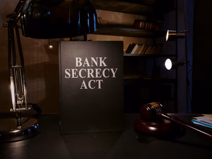 A book titled 'Bank Secrecy Act' illuminated by a desk lamp, with a judge's gavel and legal documents on the desk beside it.
