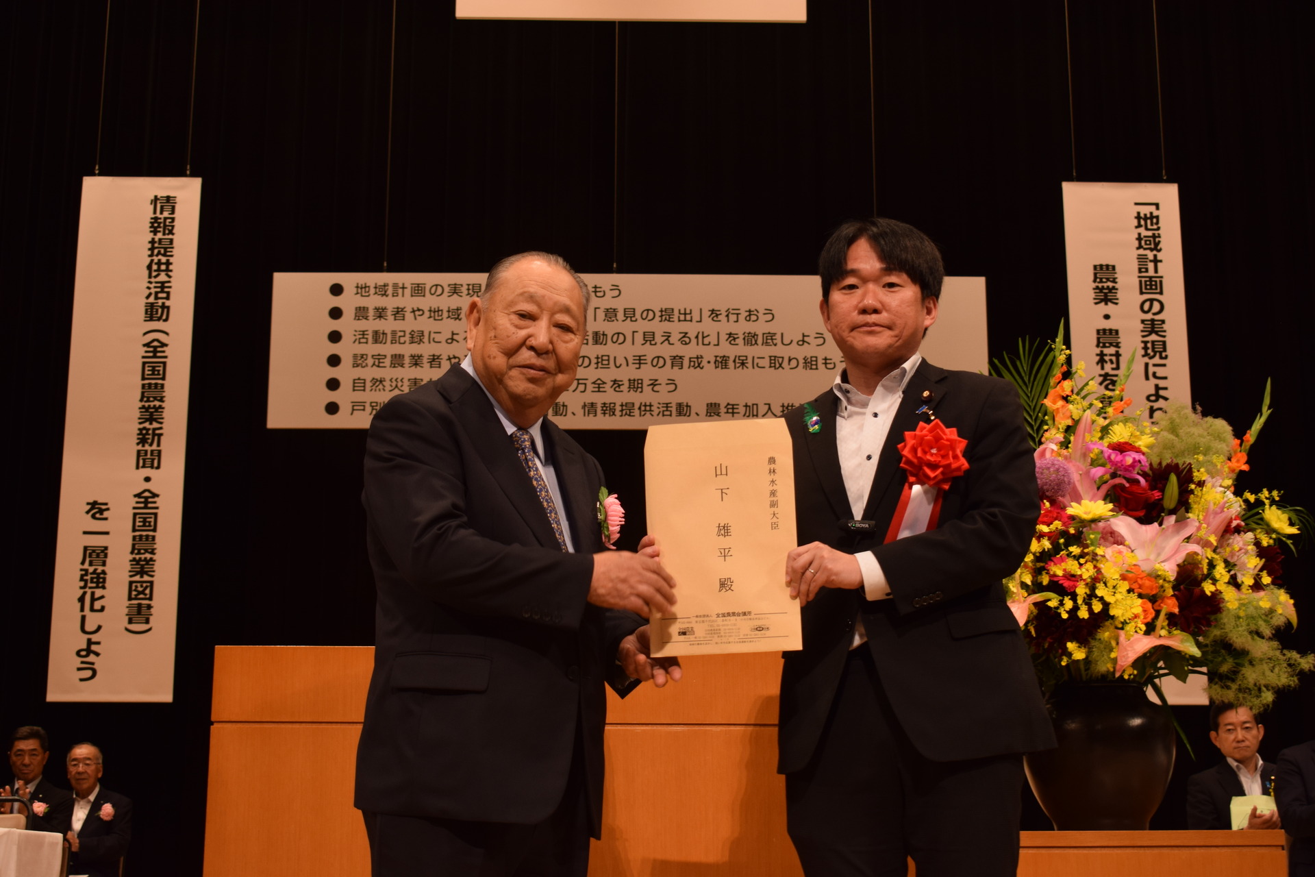 壇上で山下副大臣(右)に要請書を手渡す國井会長