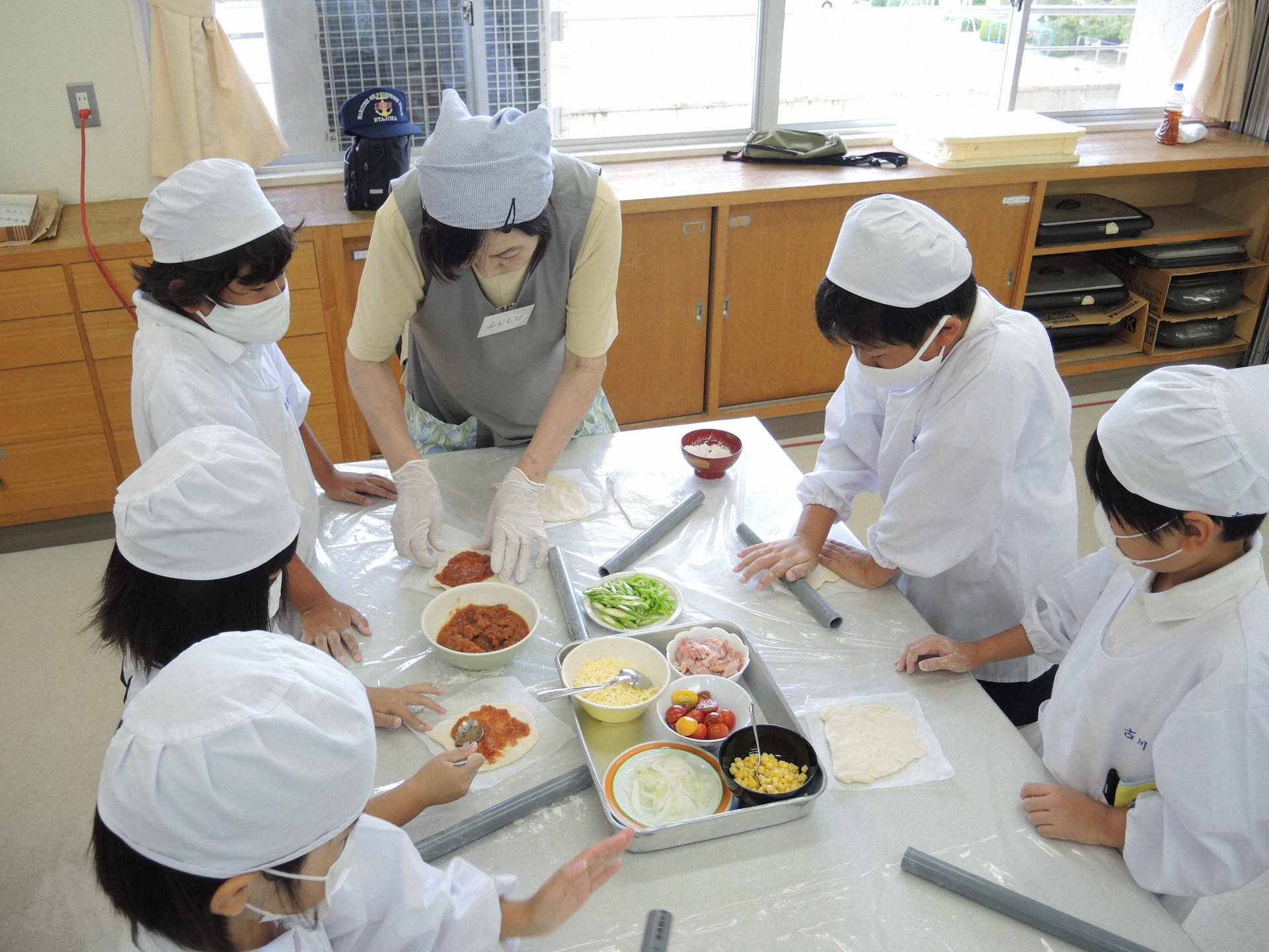 丁寧にピザ生地を伸ばしソースを塗る児童