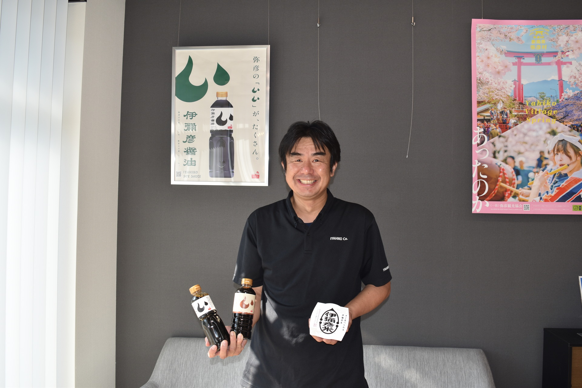 村のサテライトオフィスで伊彌彦米と伊彌彦醤油を手にする竹野代表