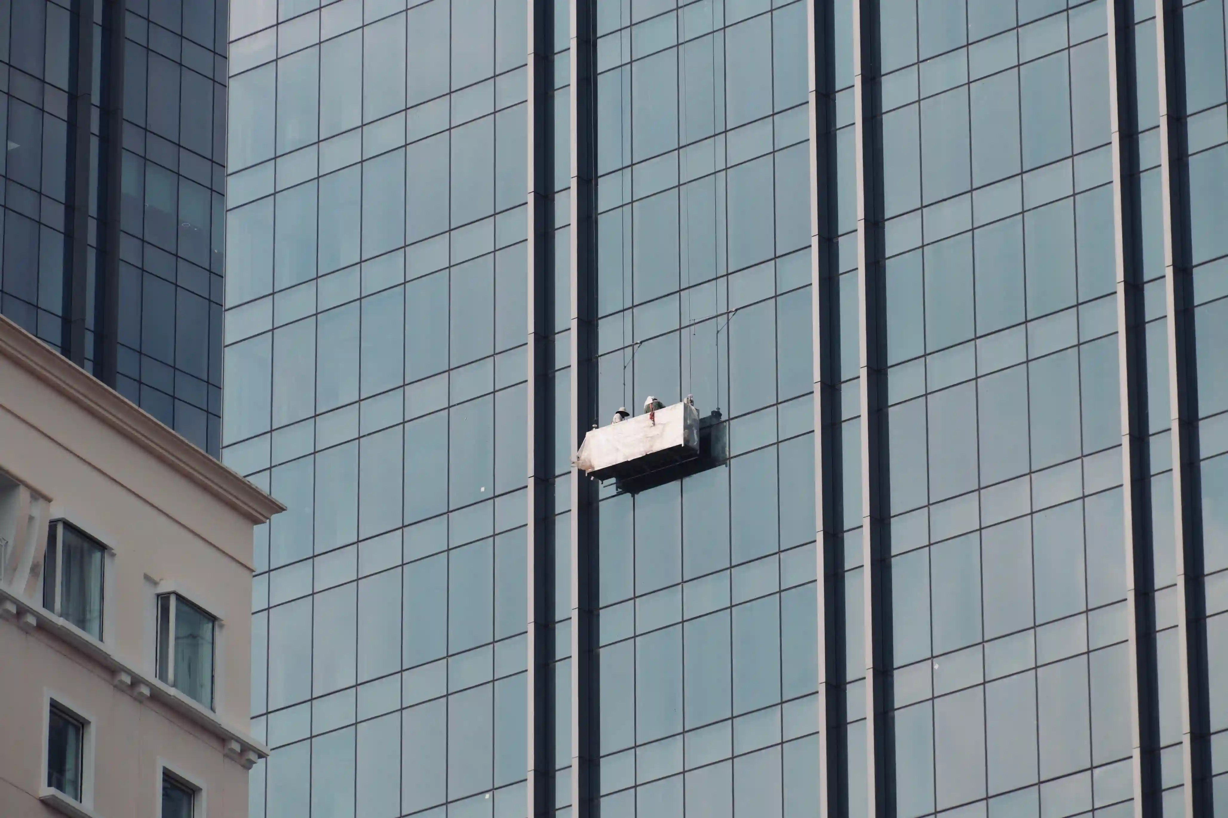 A suspended cradle carrying workers for exterior maintenance on a glass skyscraper, representing typical access methods for H3Zoom facade inspections.