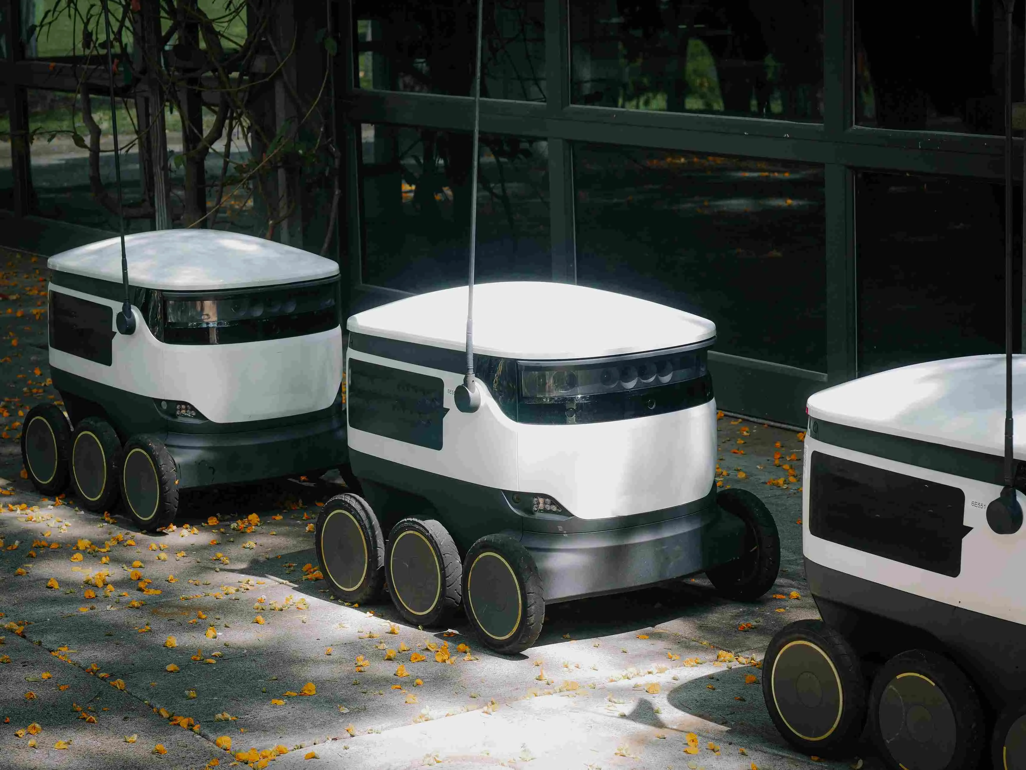 Autonomous delivery robots with wheels and antennas parked outside a building, illustrating AI automation and real-world deployment for enterprise scale operations.