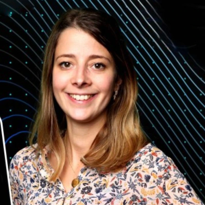 Sophie Becuwe de face, les cheveux jusqu'aux épaules, souriante, portant un chemisier