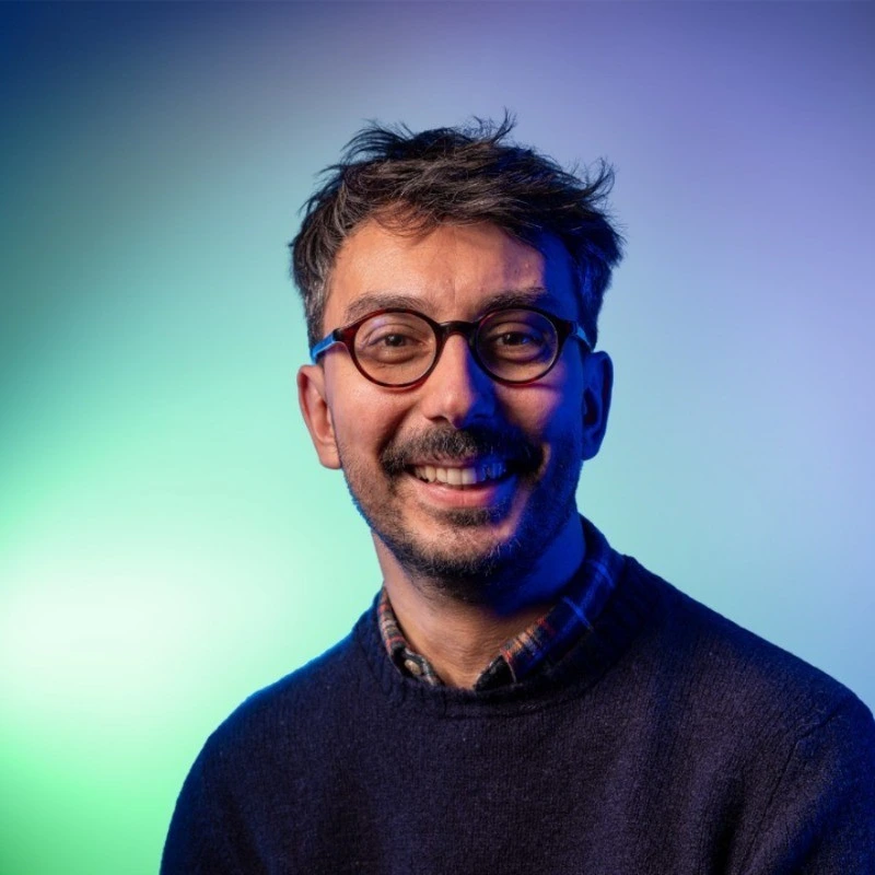 Matthieu Cesano de face, portant une chemise et un pull par-dessus, des lunettes et souriant