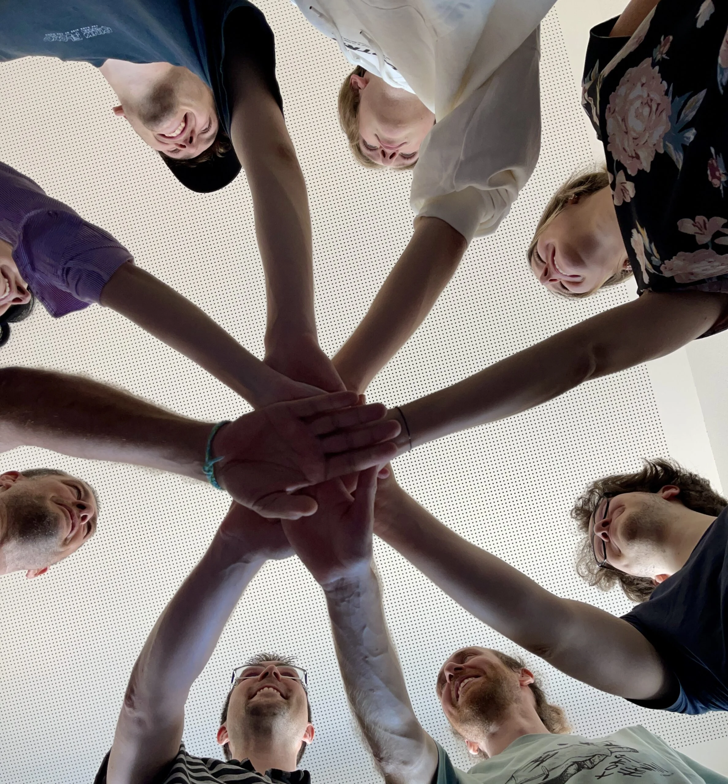 Gruppe von jungen Erwachsenen, die ihre Hände gemeinsam in der Mitte stapeln, aufgenommen aus der Vogelperspektive.