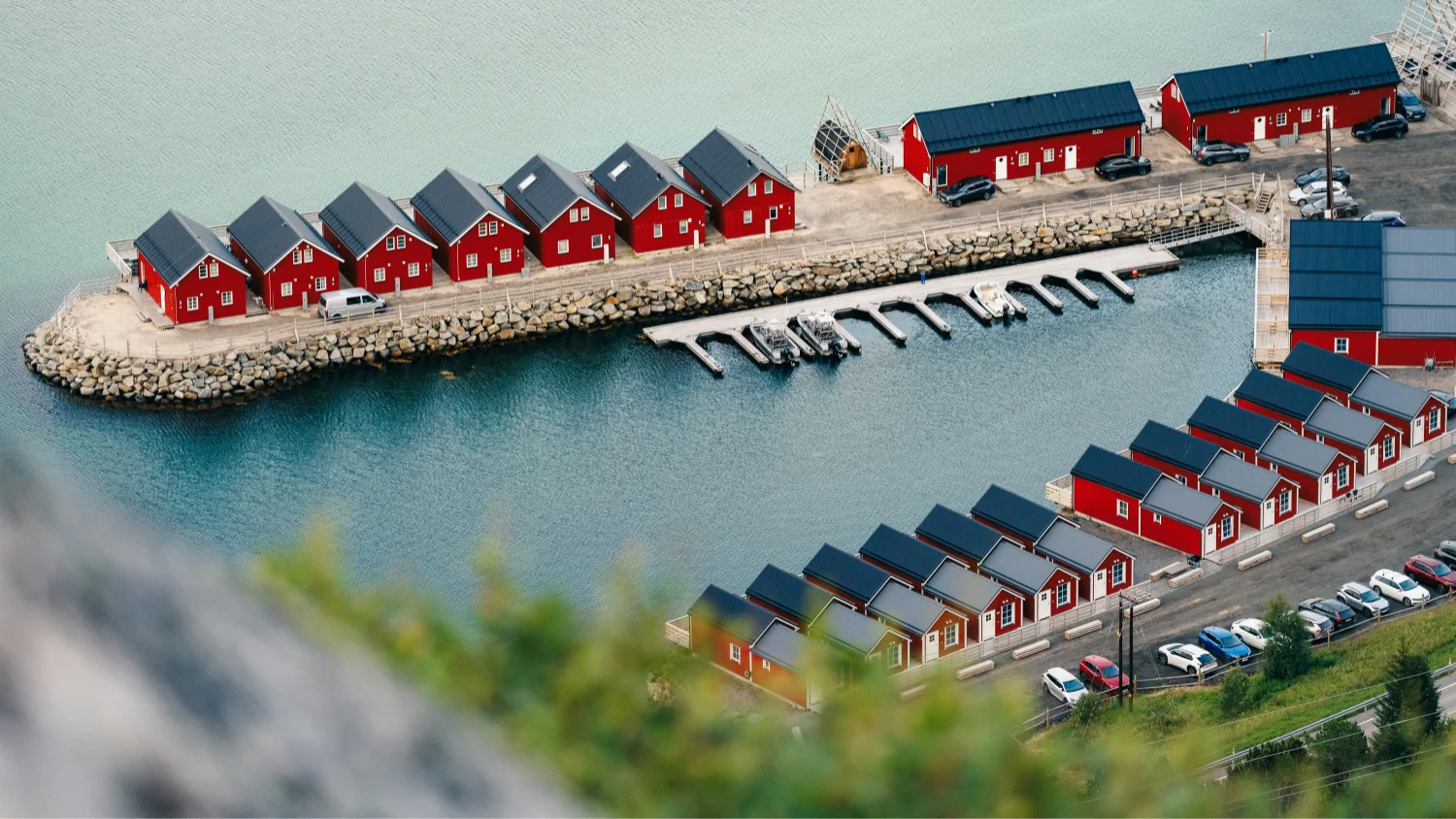 Aerial view of red wooden houses with dark roofs along a waterfront with docks and parked cars.
