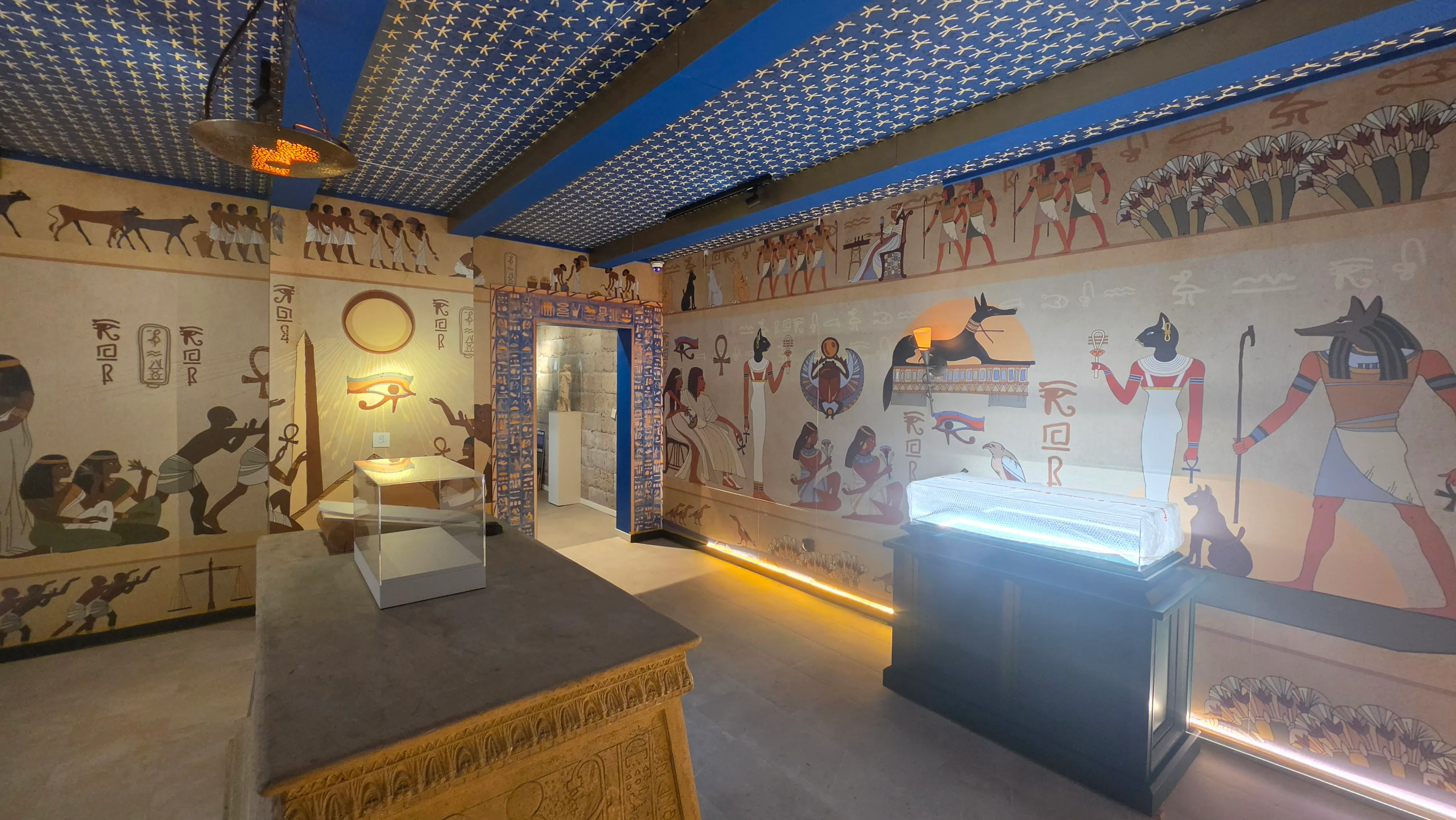 Salle de l'Égypte antique aux fresques de chats et de dieux égyptiens, vitrines éclairées au centre