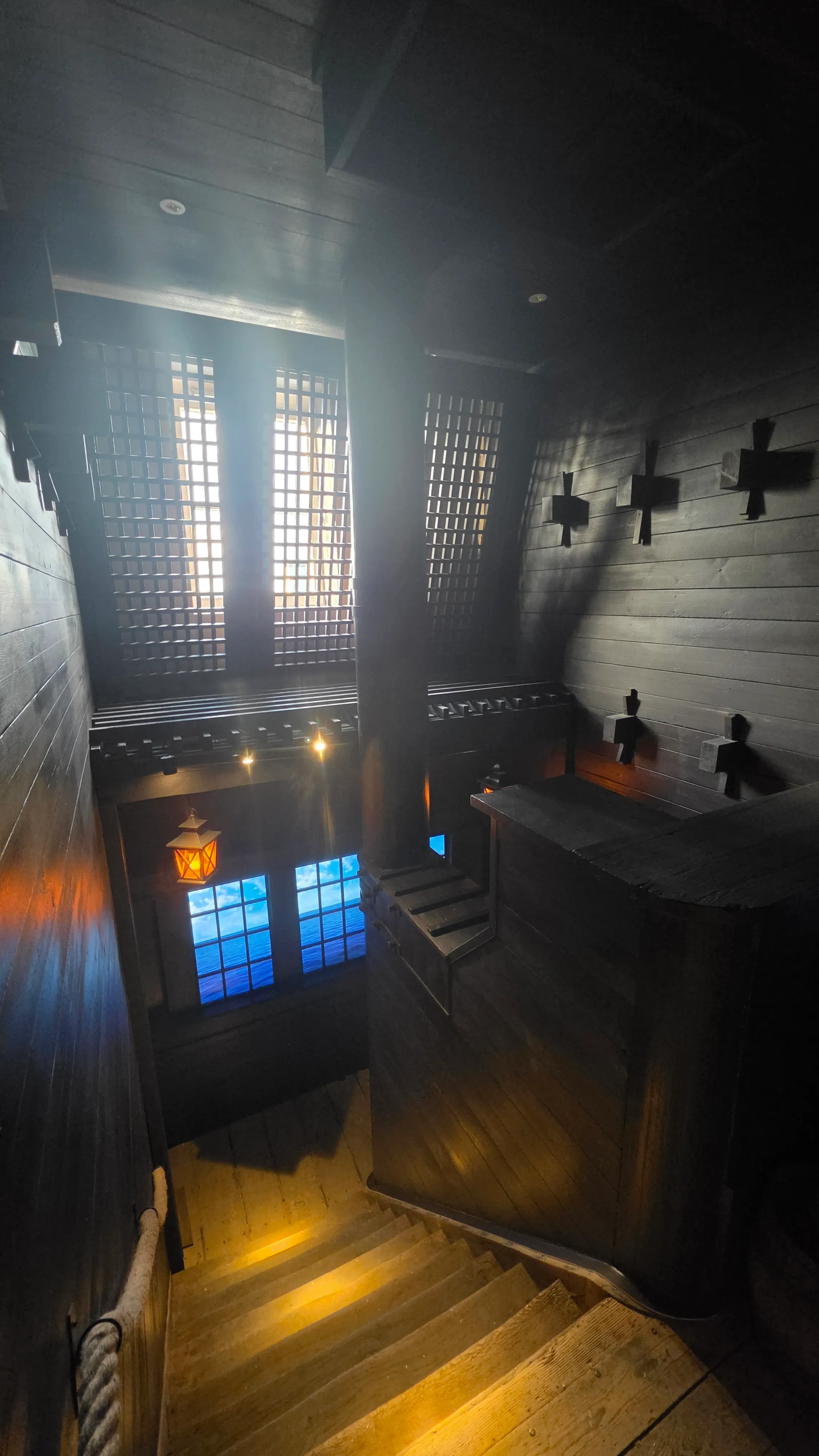 Escalier en bois sombre éclairé par des lanternes dans le décor médiéval de l'escape game La malédiction du chat noir