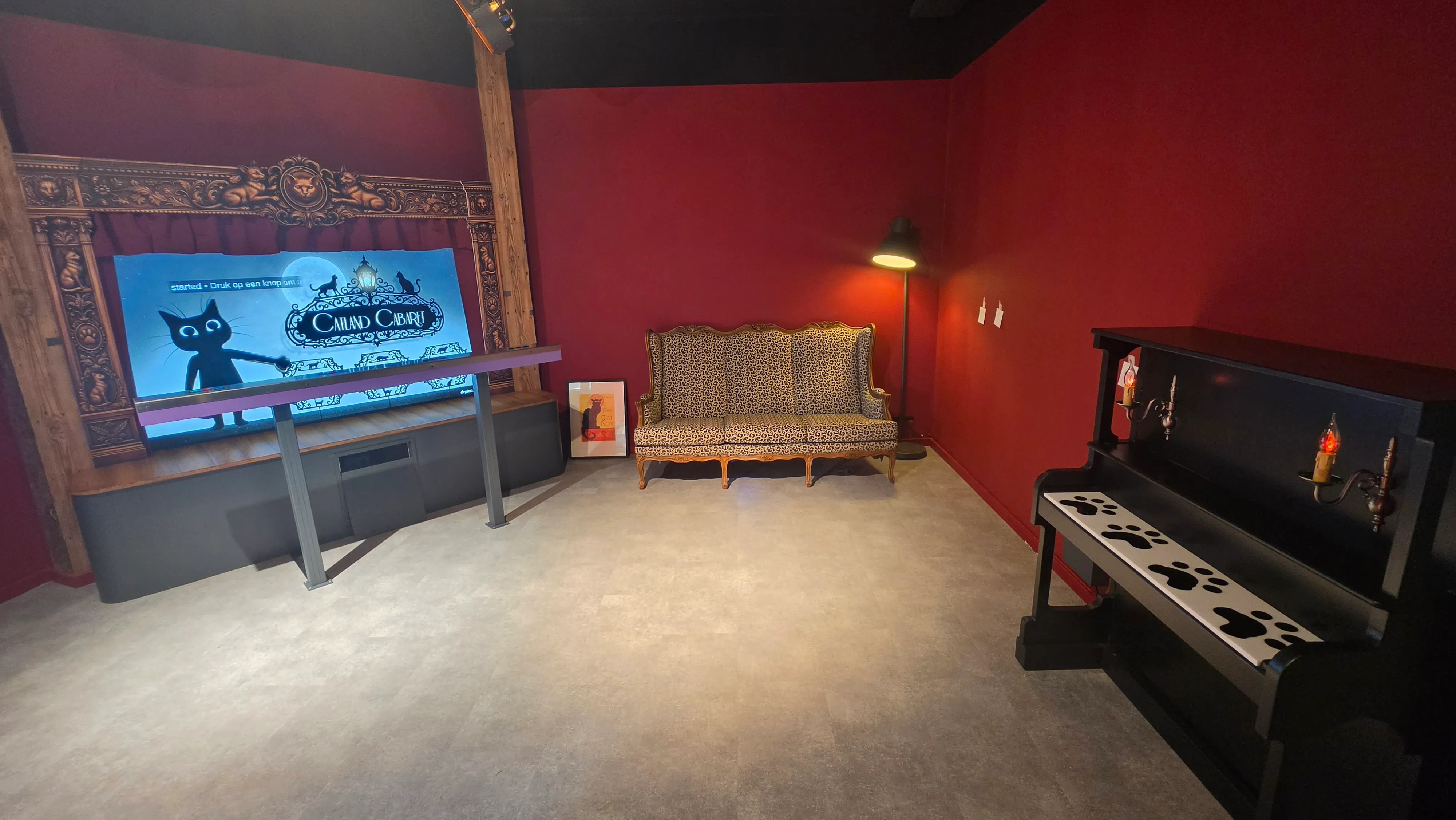 Salle rouge du Grand Cabaret avec un écran de théâtre animé, un canapé ancien et un piano aux touches en pattes de chat