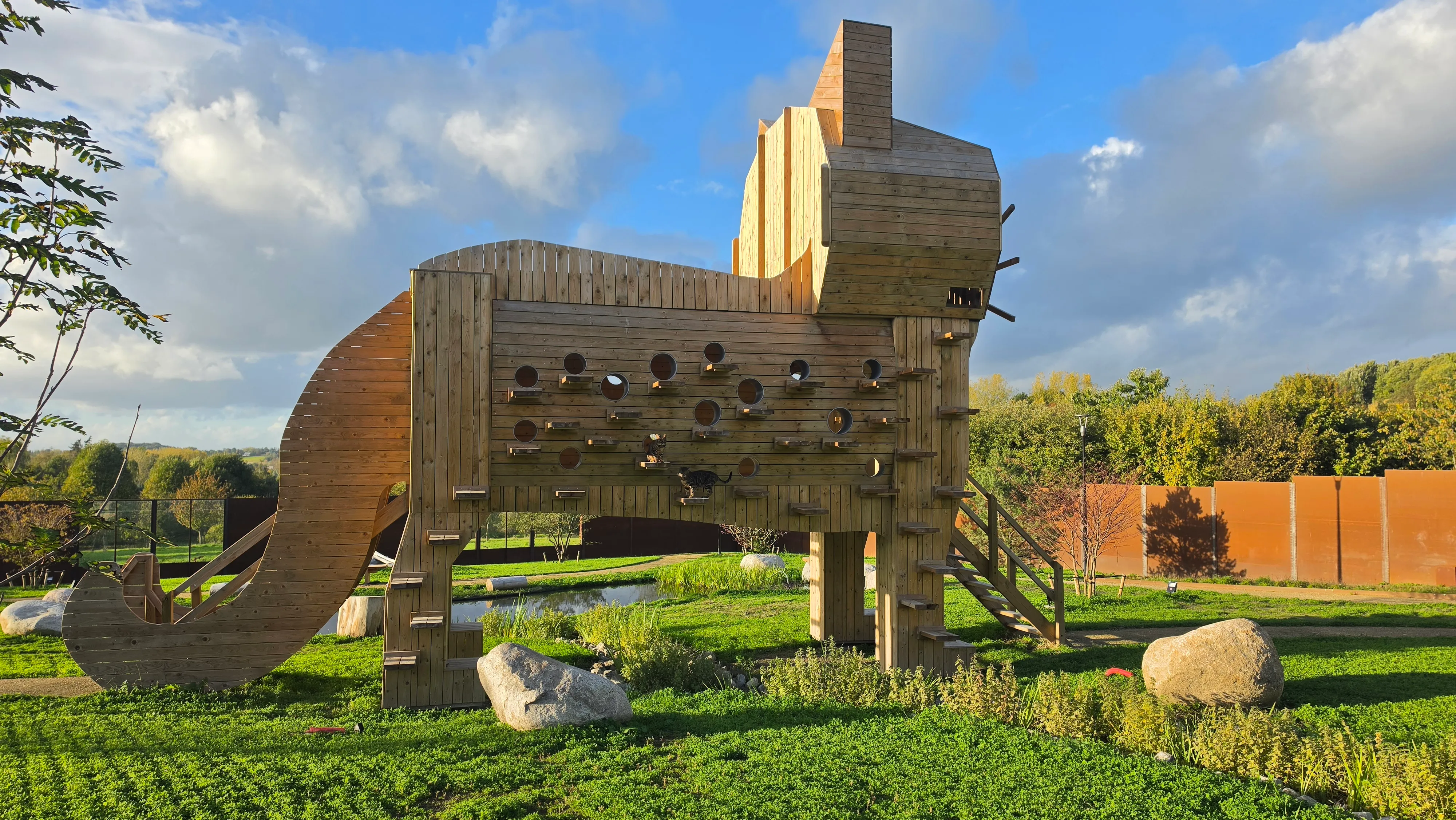 Structure géante en bois en forme de chat, percée de nichoirs, au milieu de la pelouse du parc
